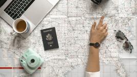 Woman pointing at map beside a passport, camera and laptop