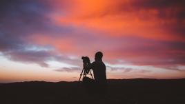 Un photographe se tient face à un coucher de soleil et le prend en photo 