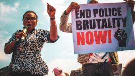 Woman and man holding a sign that reads "end police brutality now!"