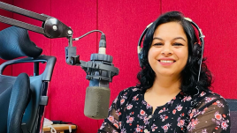 Binita Dahal with headphones on sitting in from of a podcasting microphone