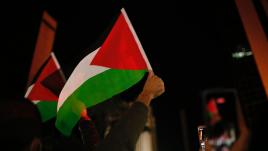 People holding phones and flags with a red sideways triangle on it and a black, white and green stripe. 