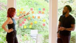 A man and a woman talking through ideas with sticky notes on a window.