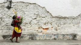 A woman carries a basket of flowers next to the cobblestone streets and crumbling walls of Antigua, Guatemala.