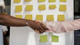 People shaking hands in front of an idea board