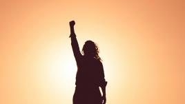 Woman holding fist aloft while silhouetted by the sun