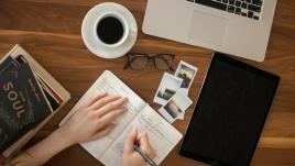 Table de travail d'un jounrliste comportant ordinateur, tablette, cahier de notes et cafe 
