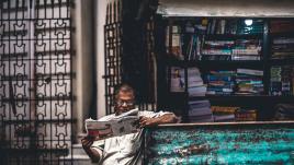 Person reading newspaper in front of a stand in India