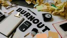 Lots of work supplies and balled up papers scattered over a desk with word burnout in the middle.