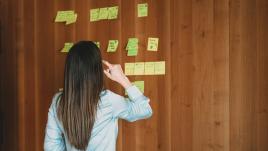A woman looking at text on sticky notes on a wall.